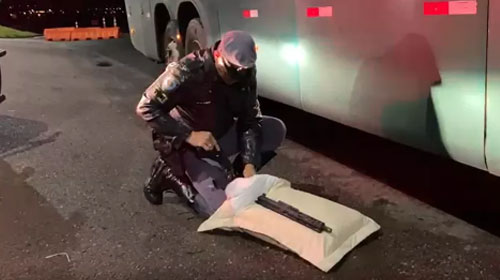 Divulgação - Policial retirando o fuzil de dentro do travesseiro que estava no ônibus com passageira - Foto: Polícia Militar Rodoviária